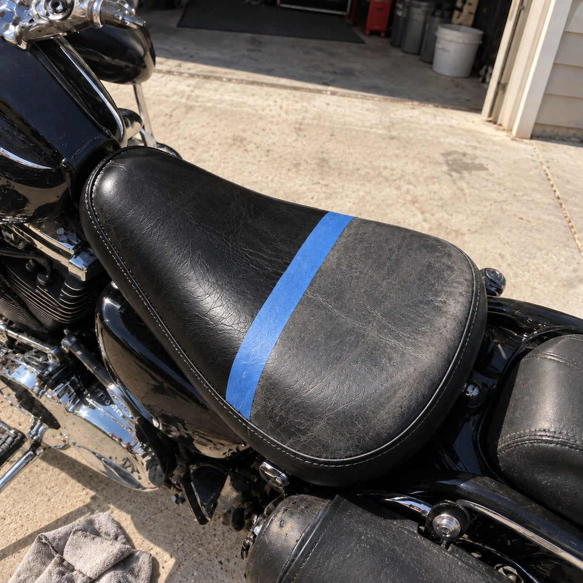 Half-done before and after on a sun-baked black leather motorcycle seat, blue tape across the middle