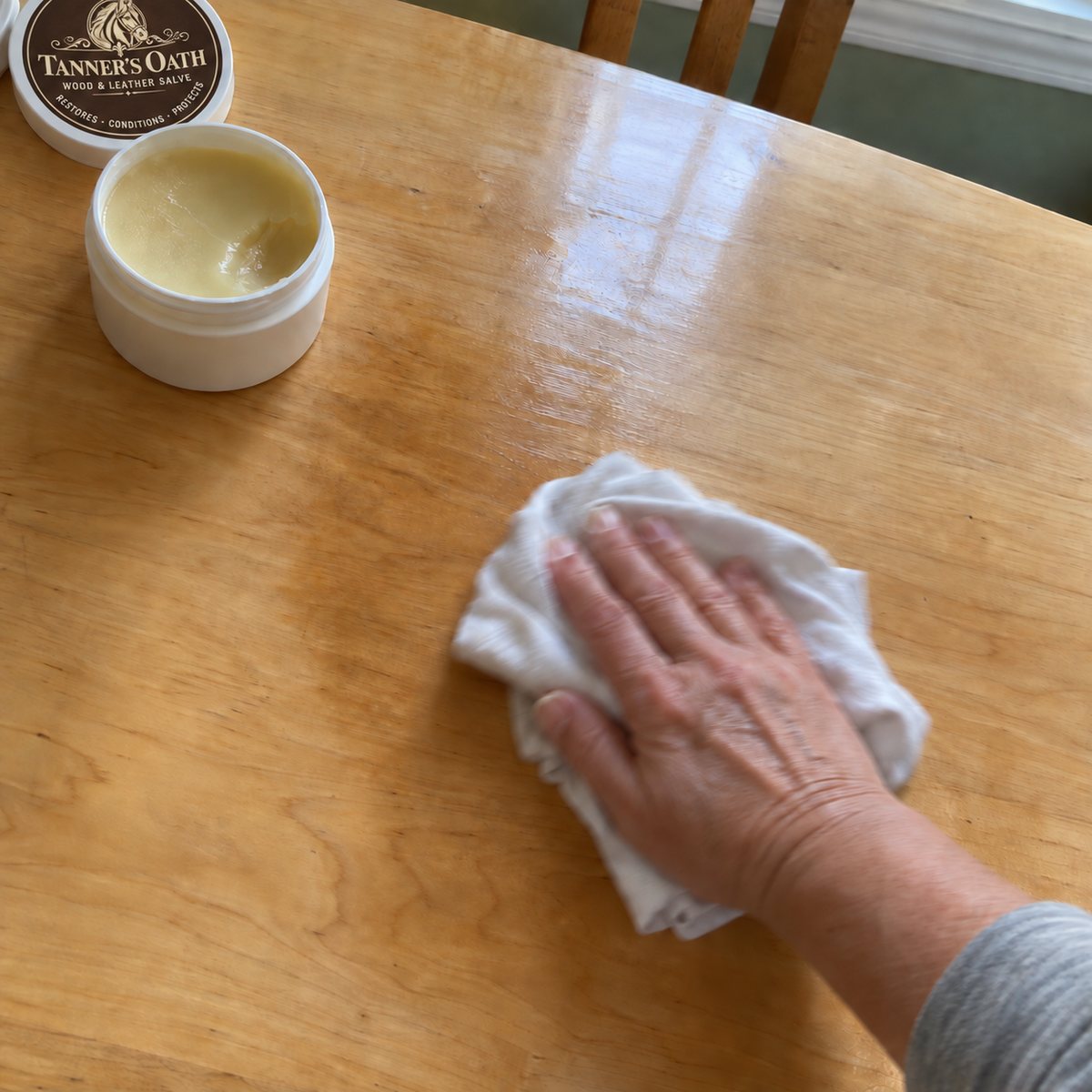 A hand rubbing Tanner's Oath into a wood tabletop with a soft cotton cloth