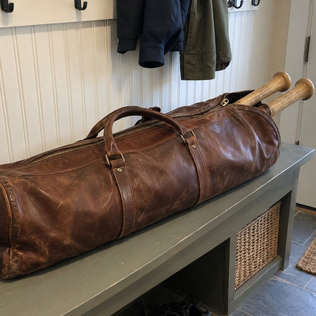 A leather bat bag on a mudroom bench with two wood bats in it