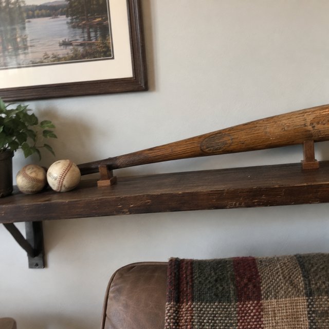 An old wood bat on a shelf with two old baseballs