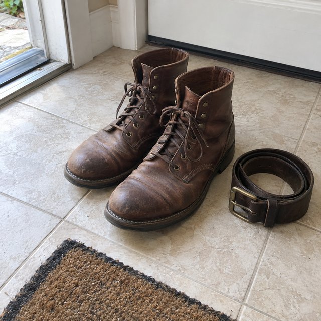 Leather work boots and a coiled leather belt by the door